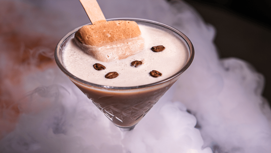 A drink presented in a martini glass, topped with a popsicle and coffee beans and surrounded by cloud of smoky mist  at Papaya Tree Hotels.