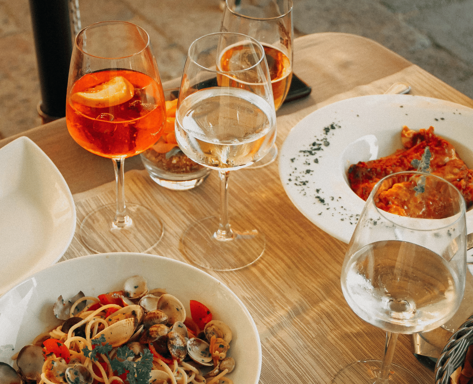 An overhead shot of a wooden table set with bowls of pasta and snacks, along with several glasses of orange and white drinks.