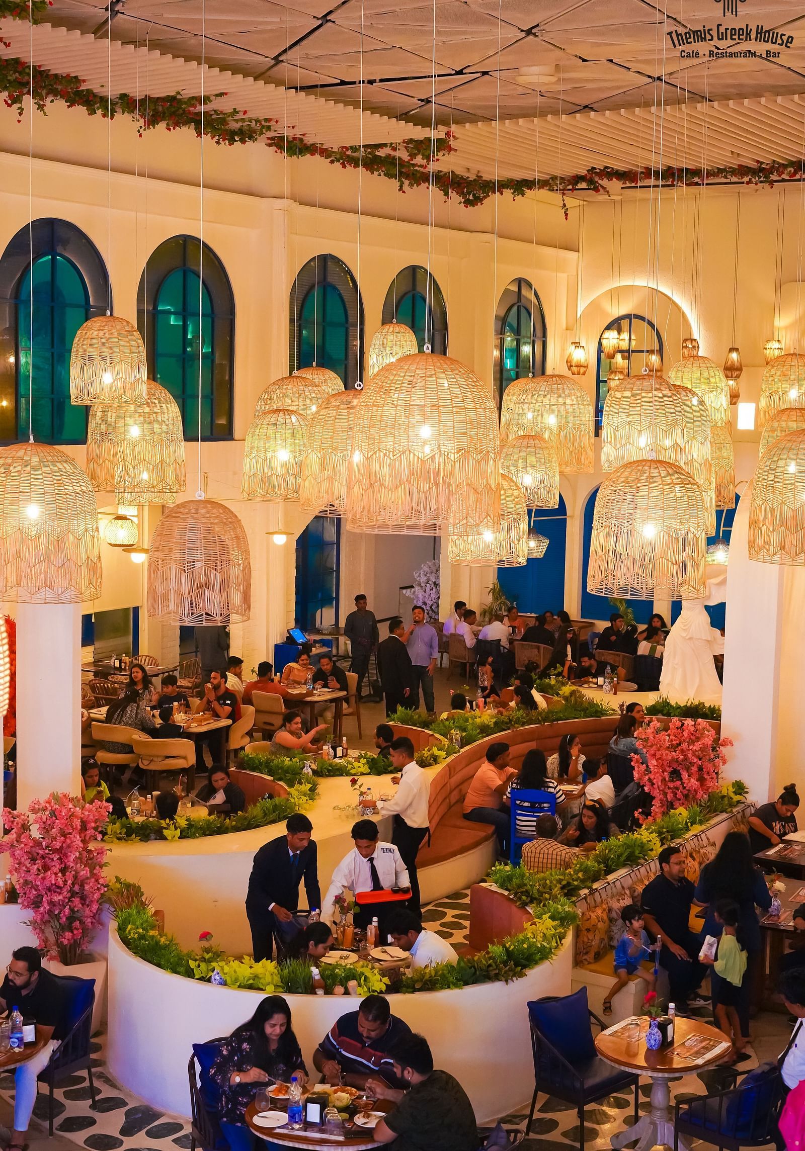 An image of a huge dining hall where people are eating and staff members are serving the dishes - Themis Barbecue House