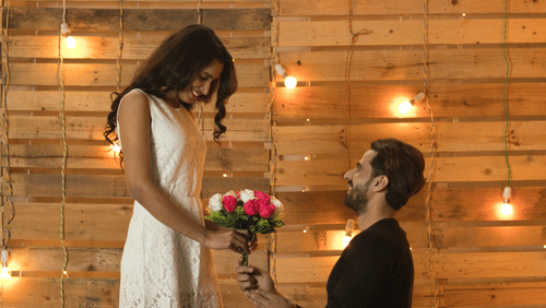 A man on his knees proposing with flowers to his fiancee.