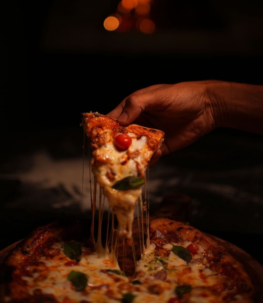 Tasteful close up of a slice of a pizza pulled out by a hand featuring loaded veggies and cheese at Rangamati Garden Resort.