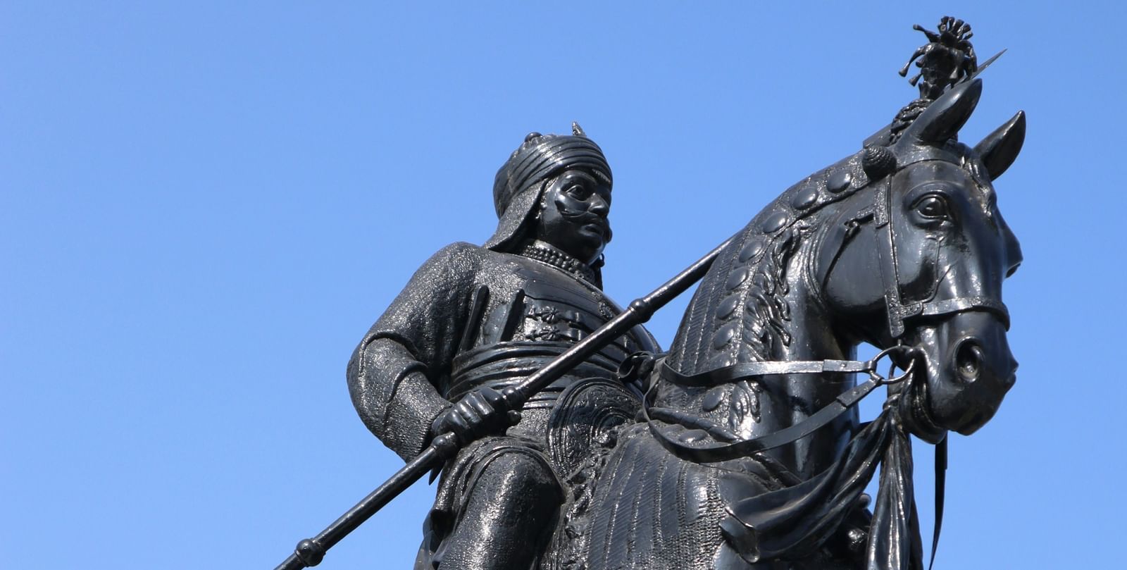 A view from below of a black painted Maharana Pratap statue on his horse Chetak.