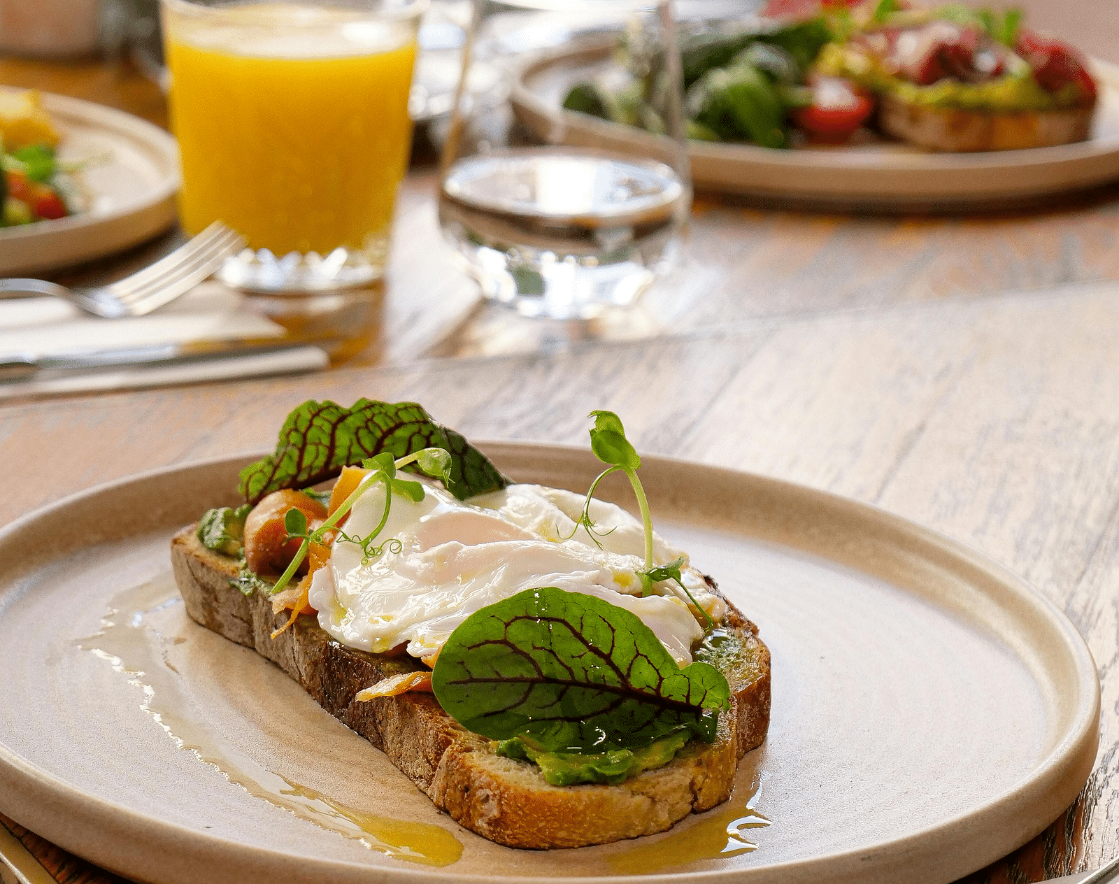 A toast with mayo placed on a plate and an orange juice in the background