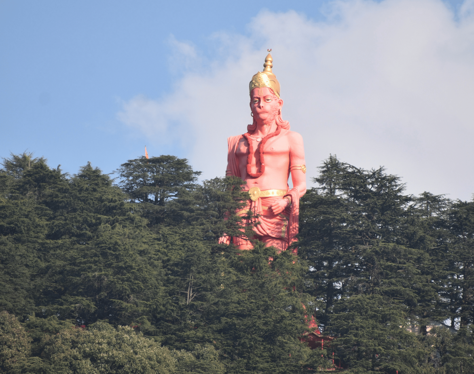 A Hanuman stupa, is visible on a forested mountain peak under a clear blue sky.
