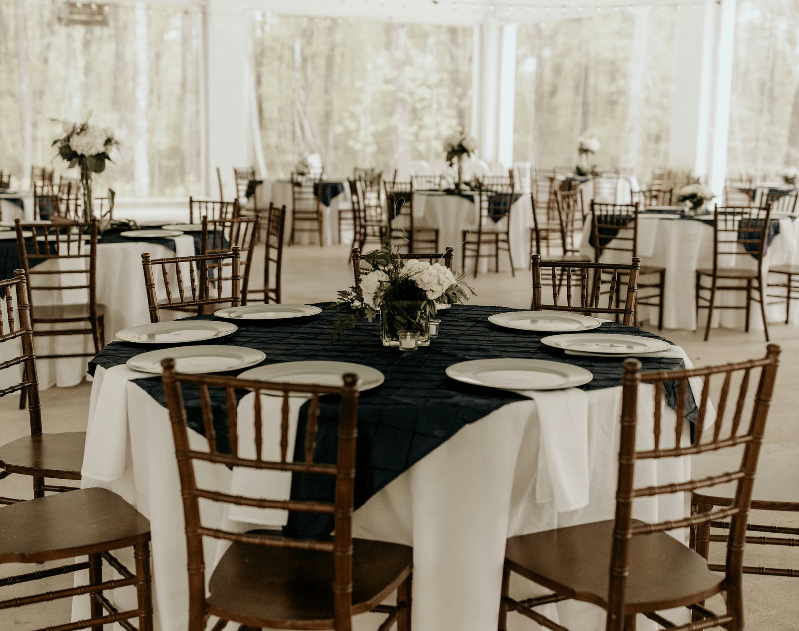 An event hall is set with white tablecloths, black runners, and dark wooden chairs.