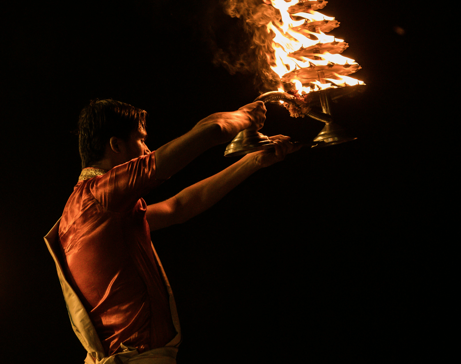 A man in traditional attire performing 'aarti' with flames flickering high in the lamp.