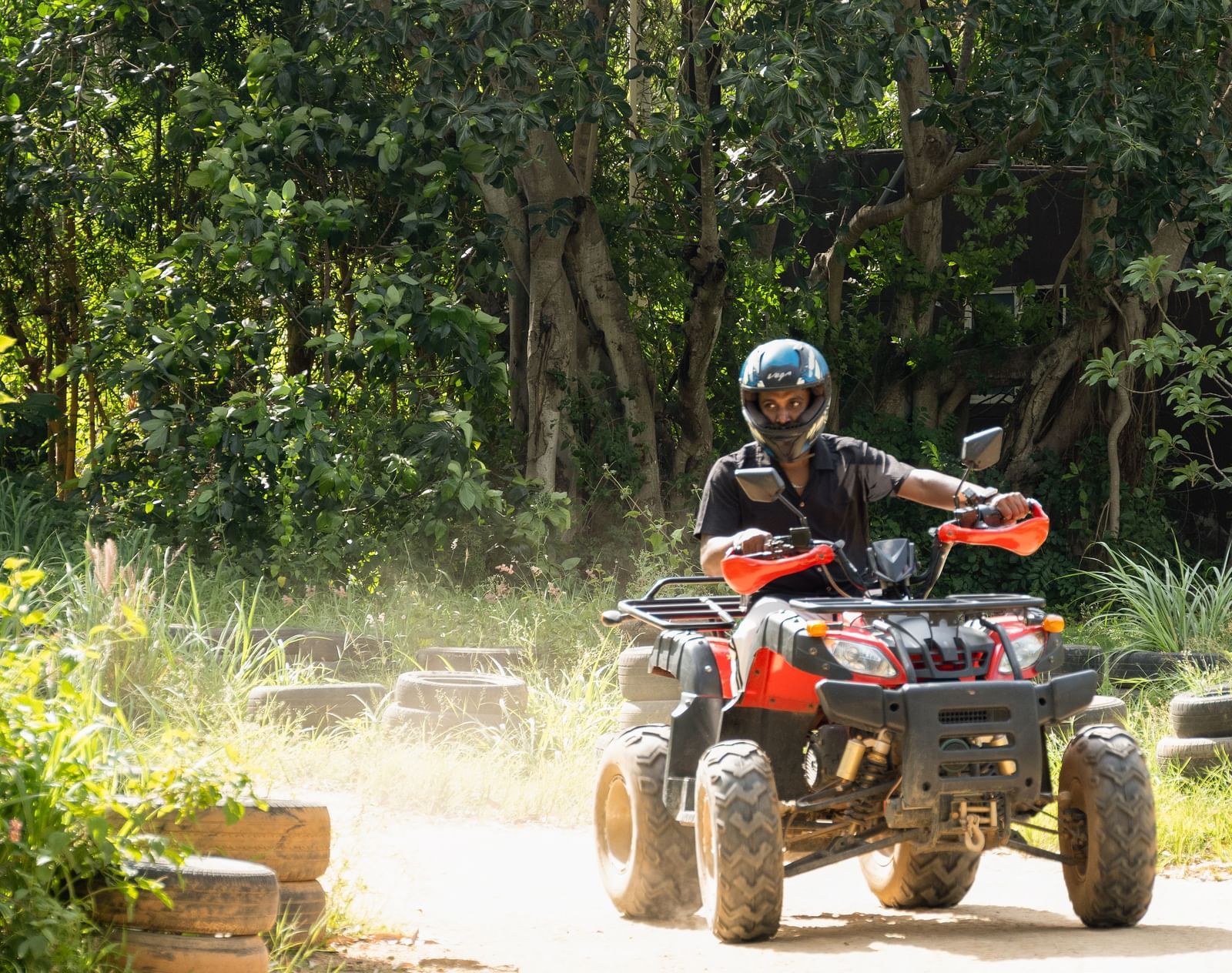 A person rides an ATV on a dirt track surrounded by trees | RD's Nature Retreat, Bangalore