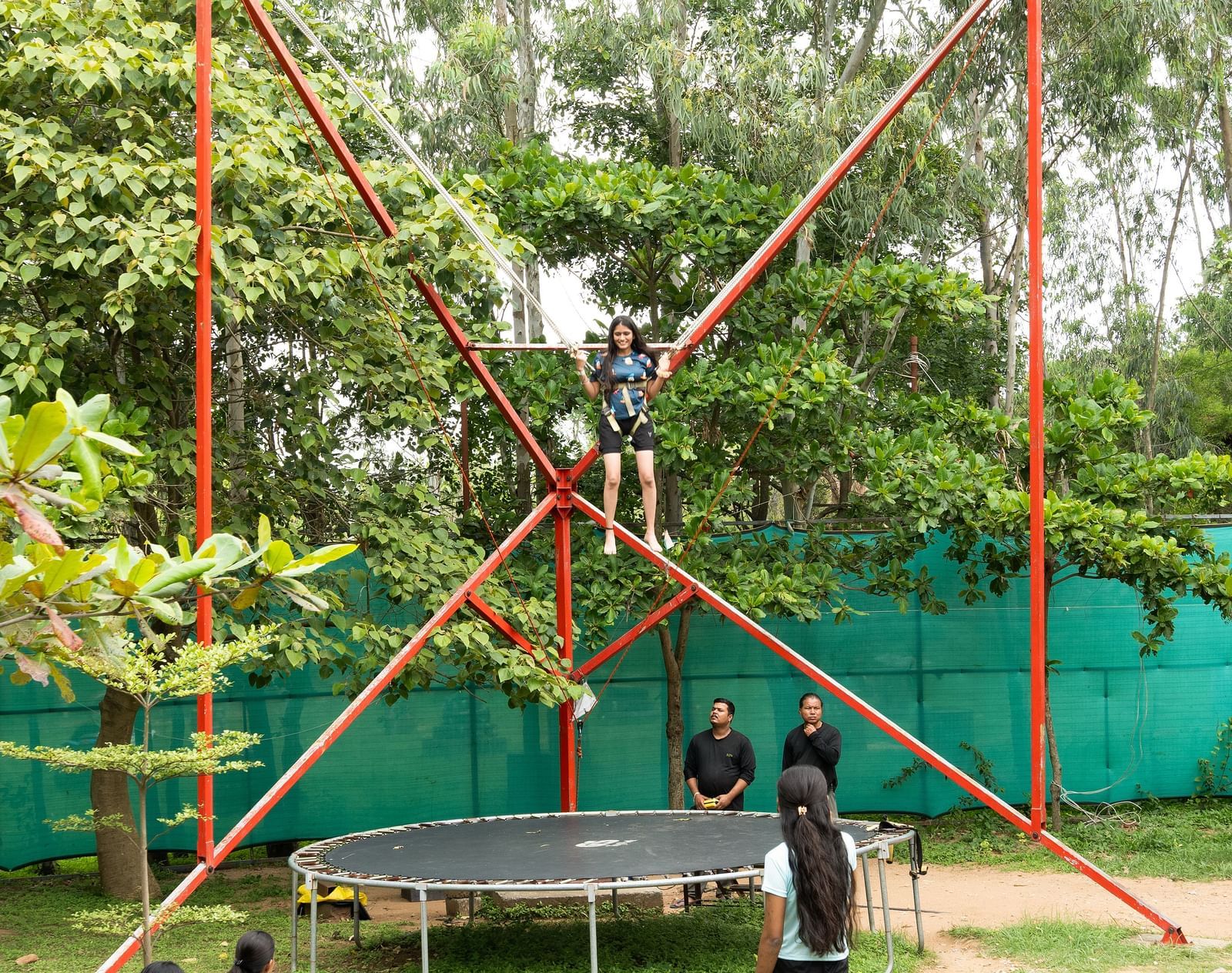 People are engaged in a bungee trampoline activity in an outdoor setting with trees | RD's Nature Retreat, Bangalore