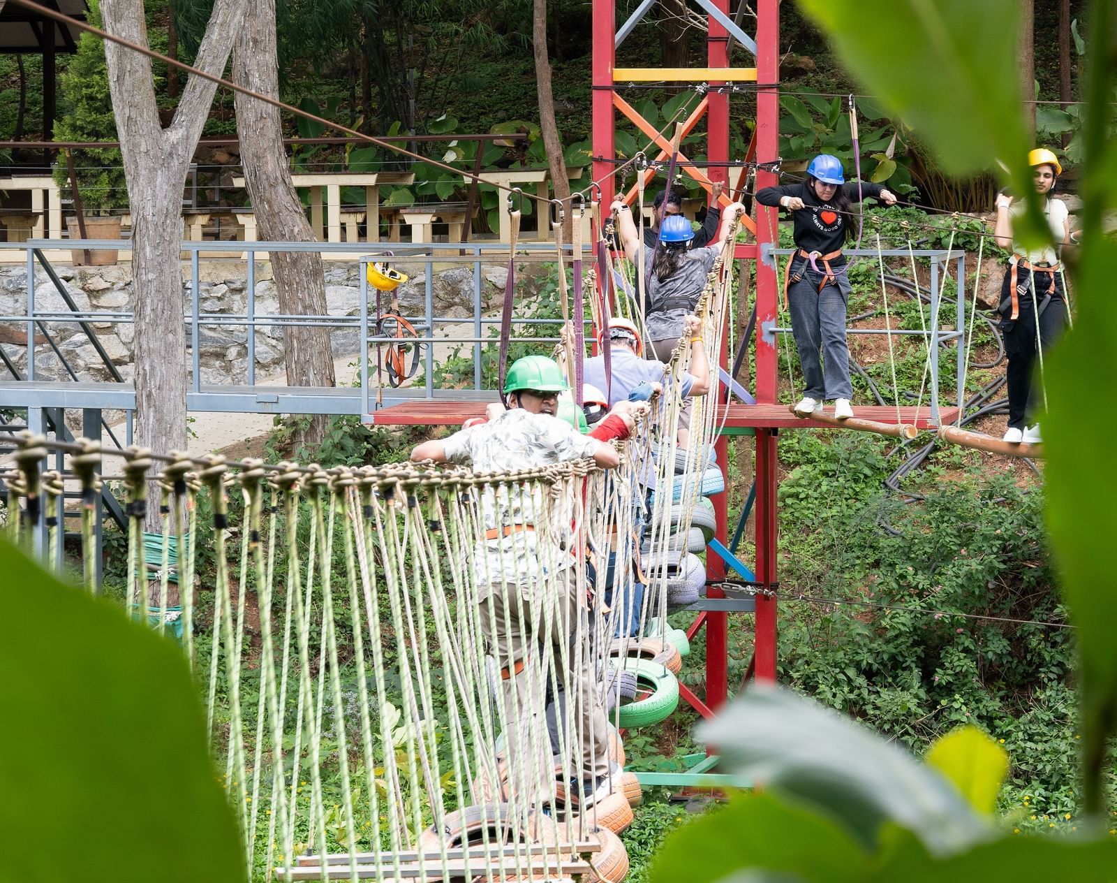 A wooden structure with ropes and a bridge-like element is visible in a green, outdoor setting | RD's Nature Retreat, Bangalore