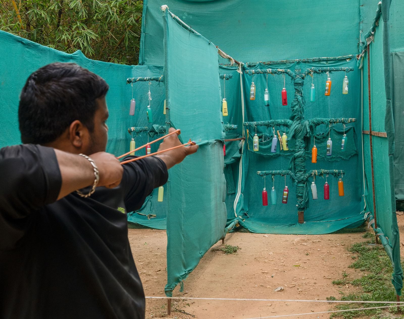 A person stands in a sheltered area, holding what appears to be a paintball gun, aiming forward | RD's Nature Retreat, Bangalore