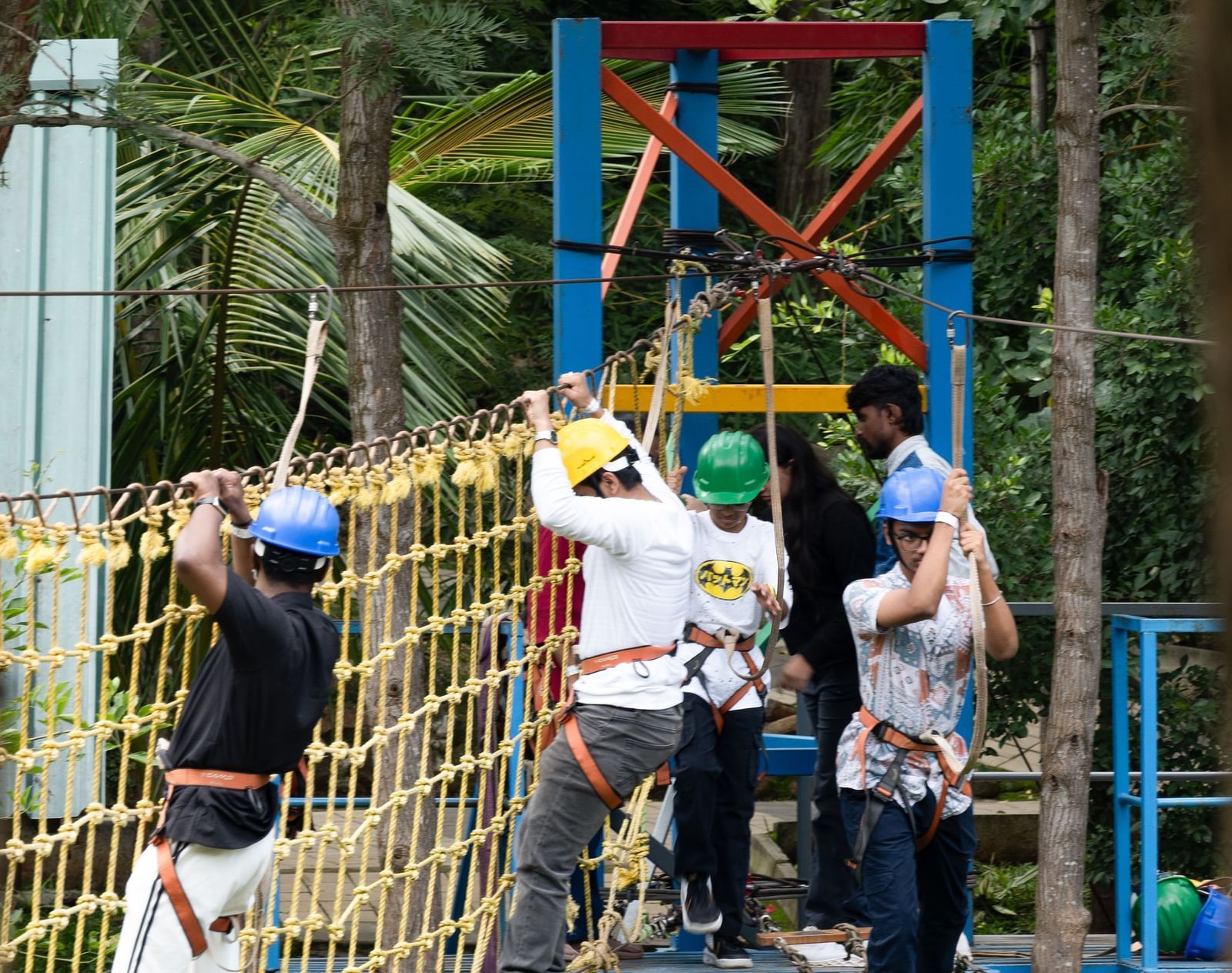 People are engaged in activities on a multi-level adventure structure with ropes and platforms | RD's Nature Retreat, Bangalore