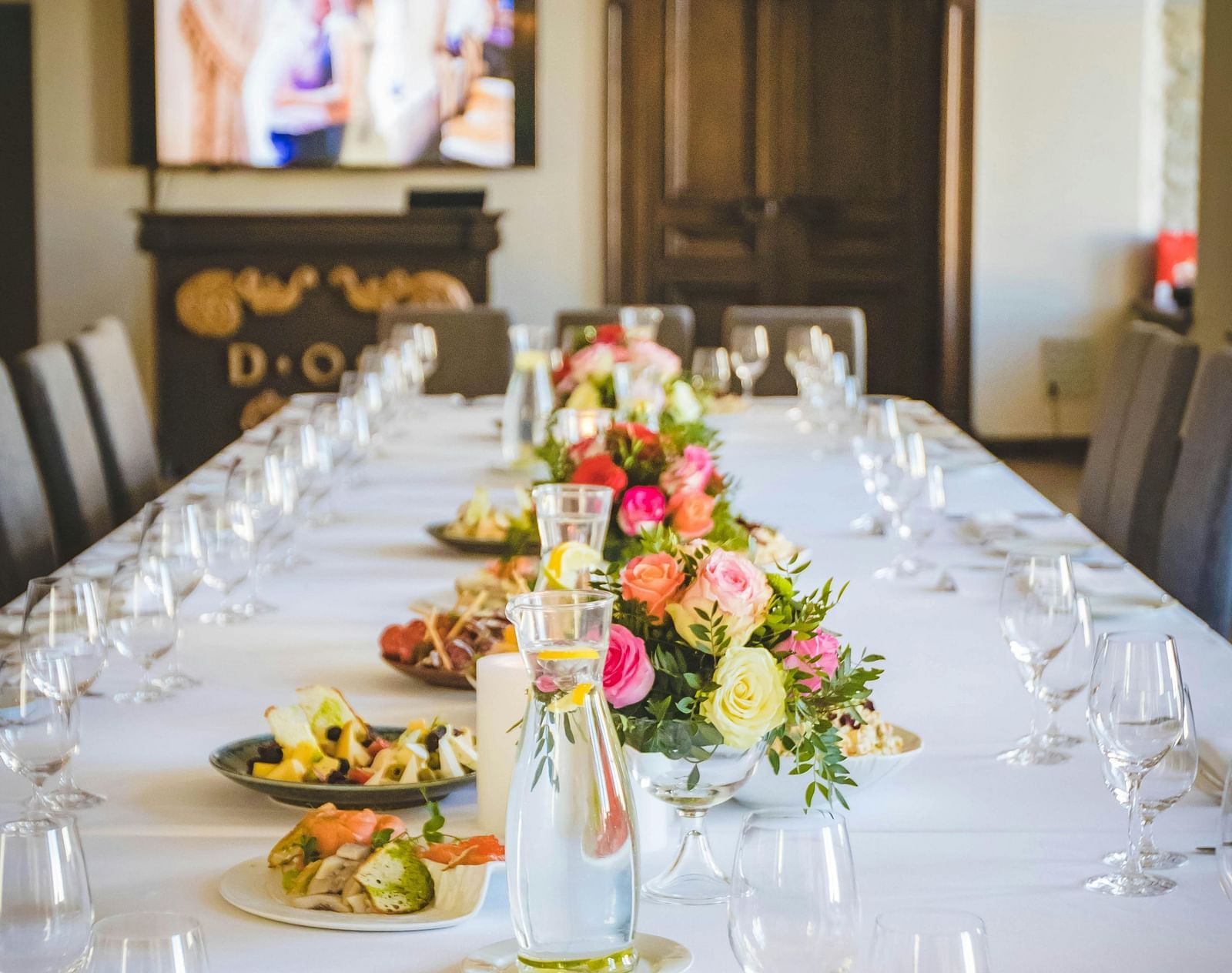 A long dining table decorated with flowers in the middle along with shiny glassware and cutlery set on the table.