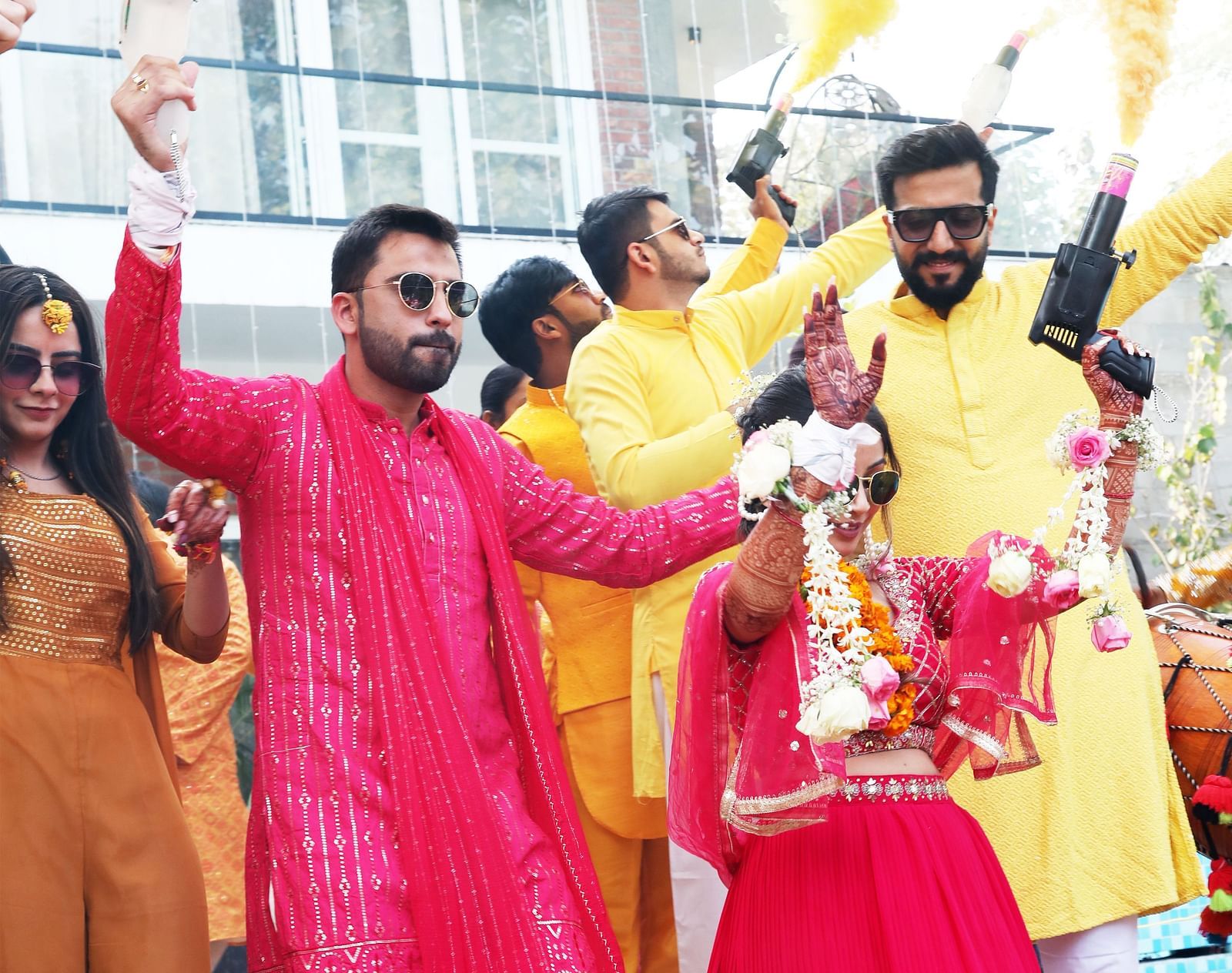 Guests in festive attire celebrating with color powder outside the building at Tisya Farms, Gurgaon.