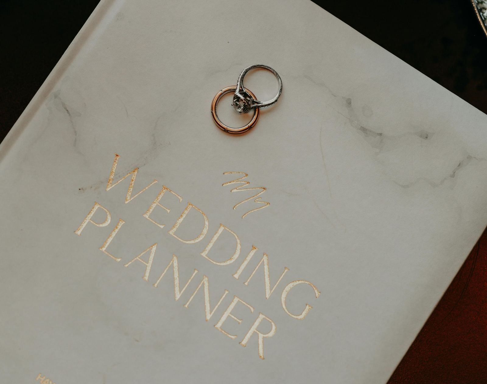 A close-up of a marble-textured wedding planner book with two wedding rings placed on its cover.