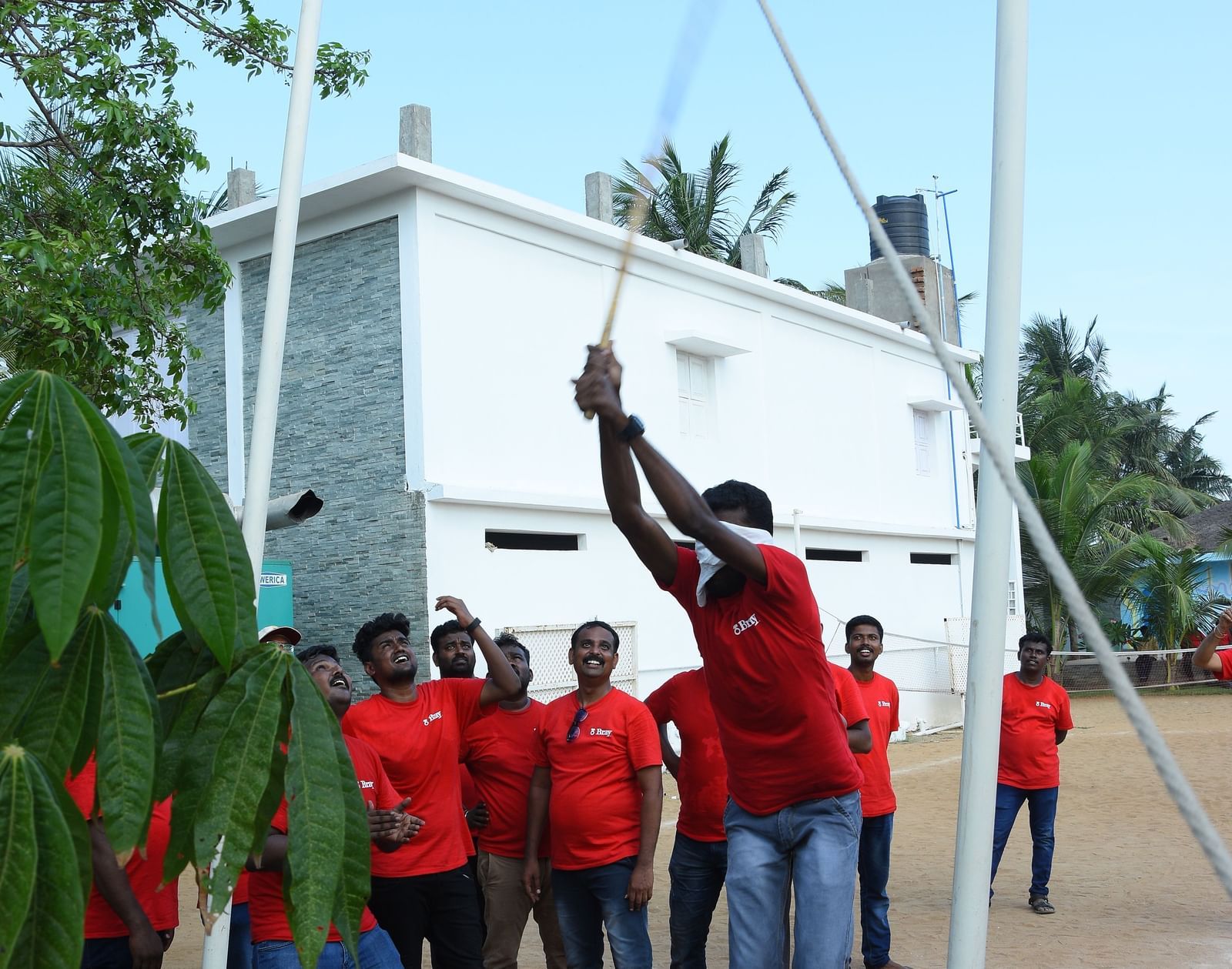 A person breaking a clay pot with blindfolds and a group of people looking at him in an outdoor area at Grande Bay Resort & Spa.