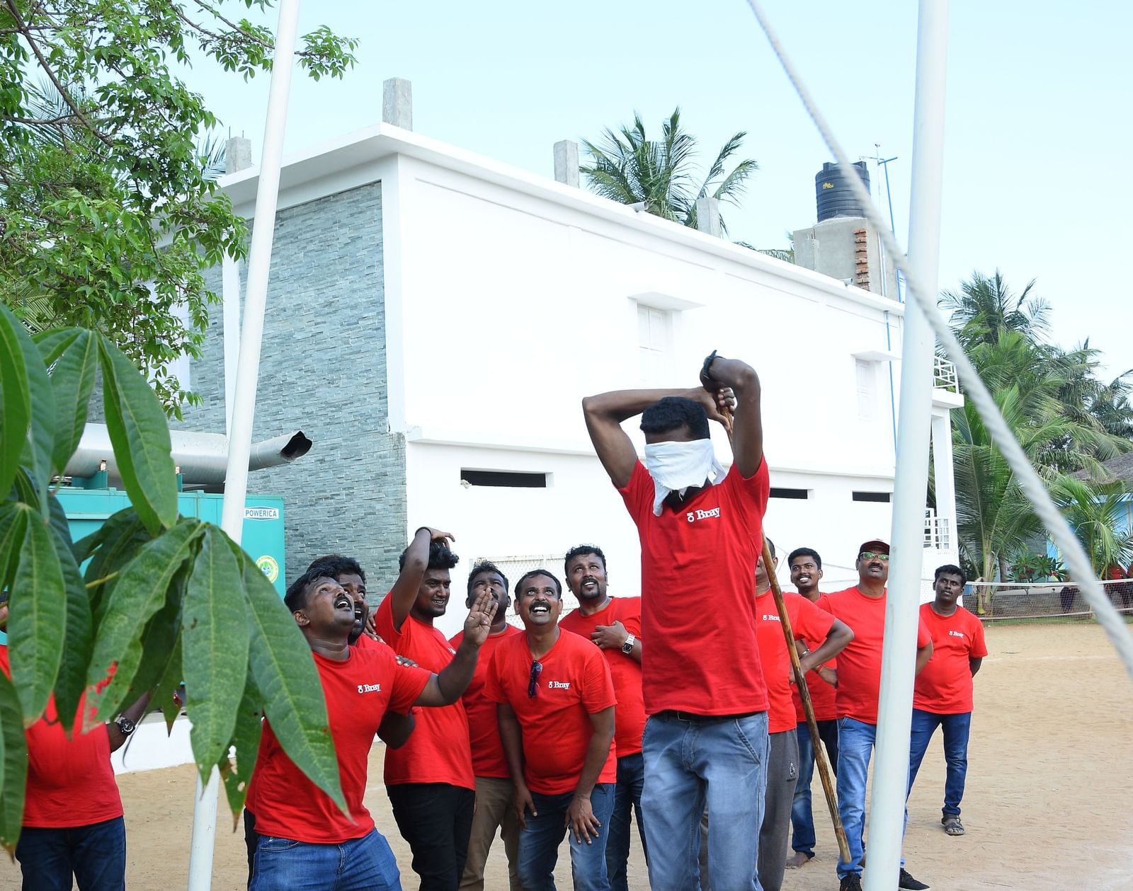 A person trying to break a clay pot with other people at the background in an outdoor area at Grande Bay Resort & Spa.
