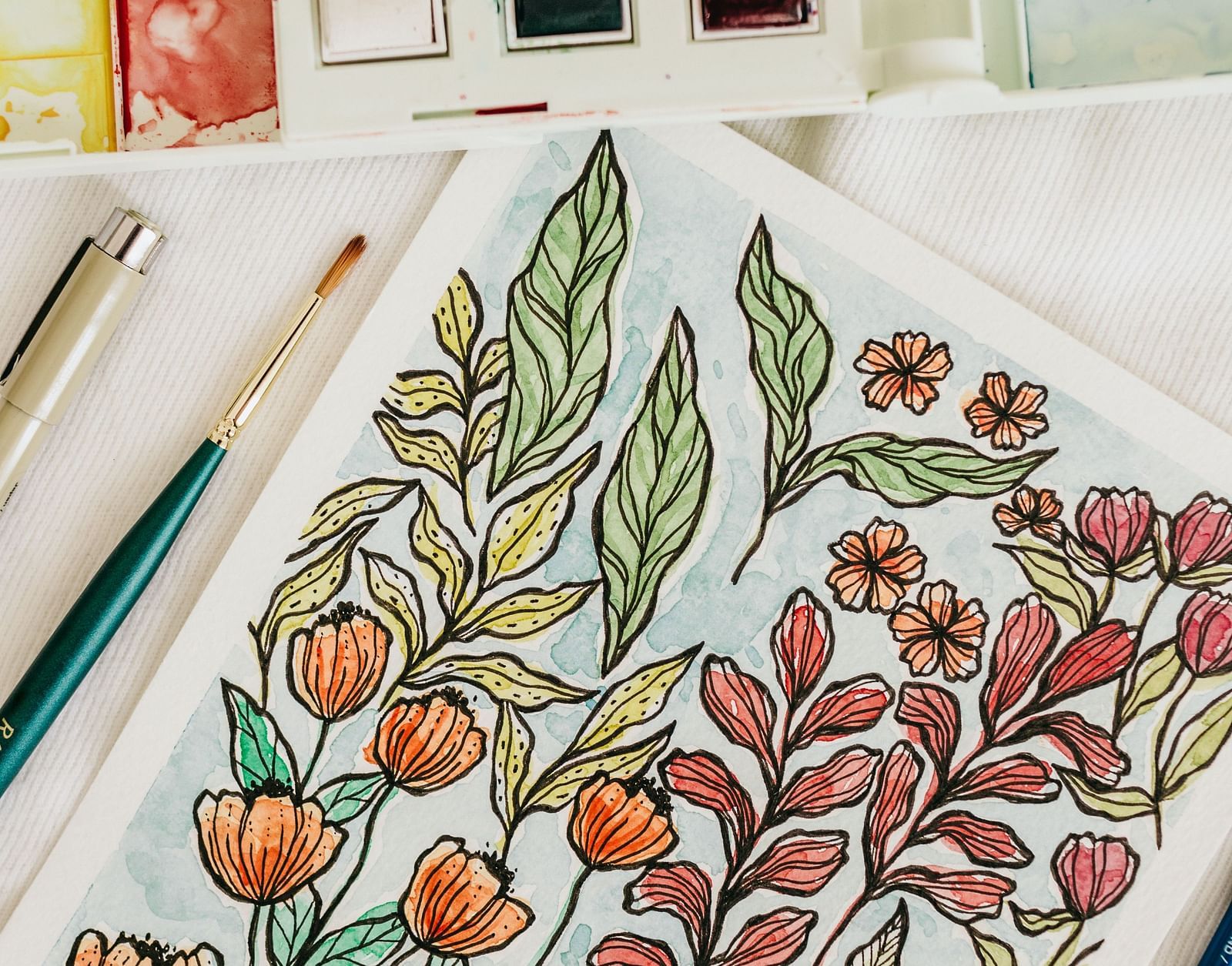 a notebook with a painting with colours and brush on the side 
