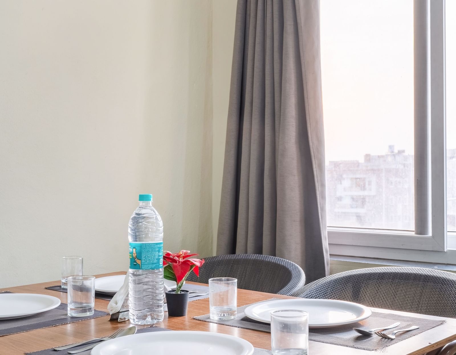 A close-up of a dining table set with bottled water and plates, beside a window.