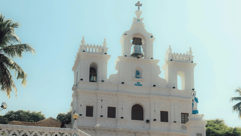Whitewashed church with twin bell towers and palm trees in the foreground.