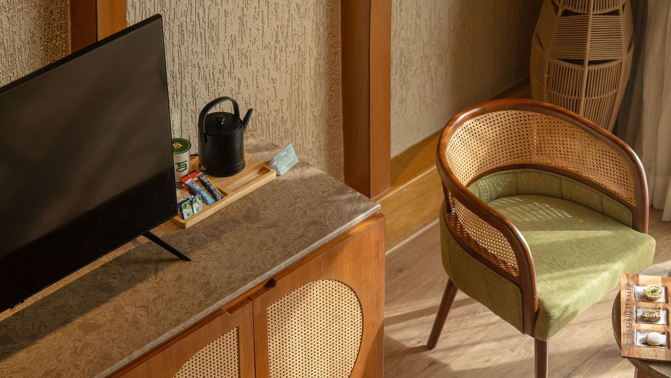 Flat-screen TV and writing desk setup next to a comfortable chair and cabinet at Ananta Spa and Resort, Ajabgarh.
