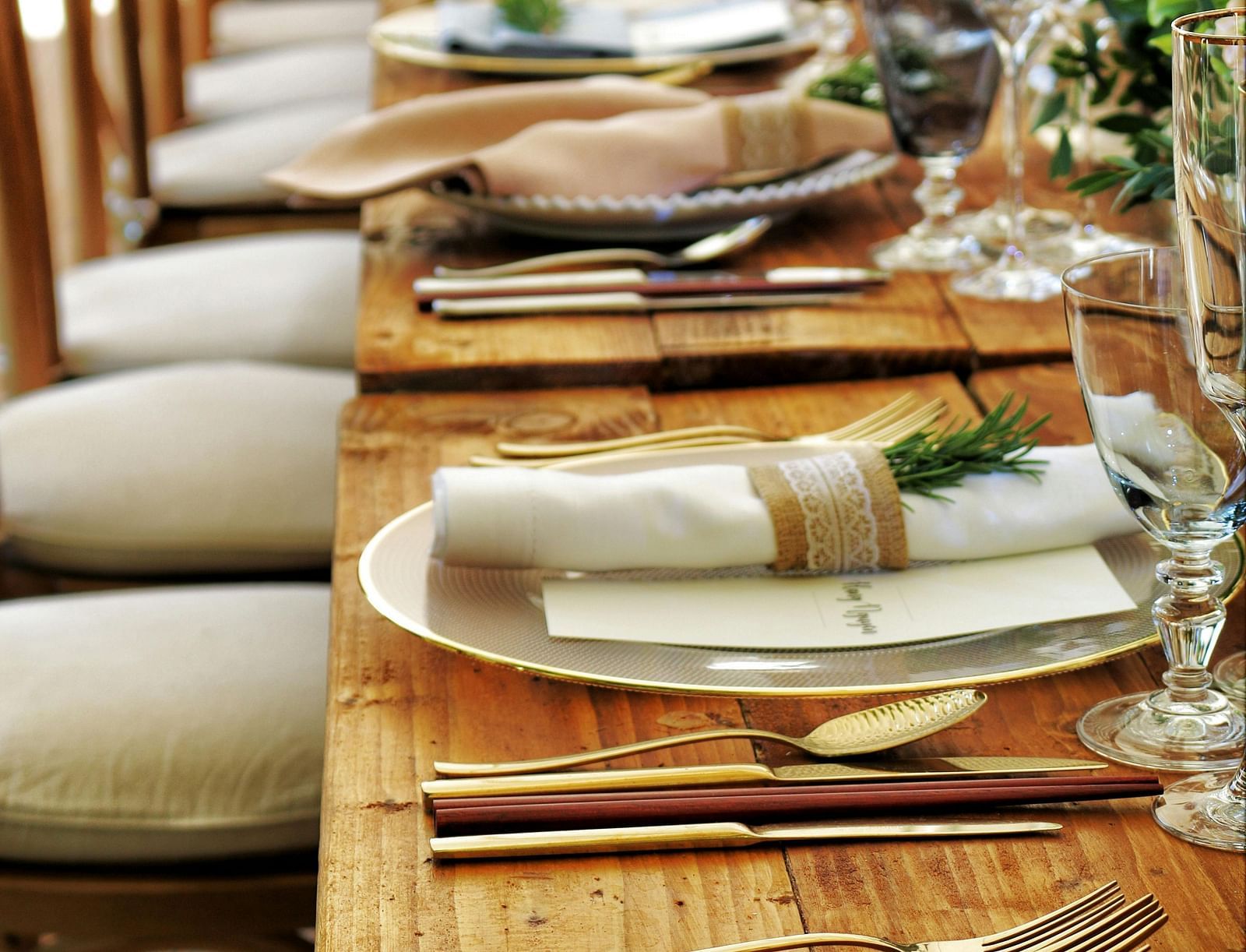 A long wooden table with beautifully set cutlery with small fern leaves in vases.