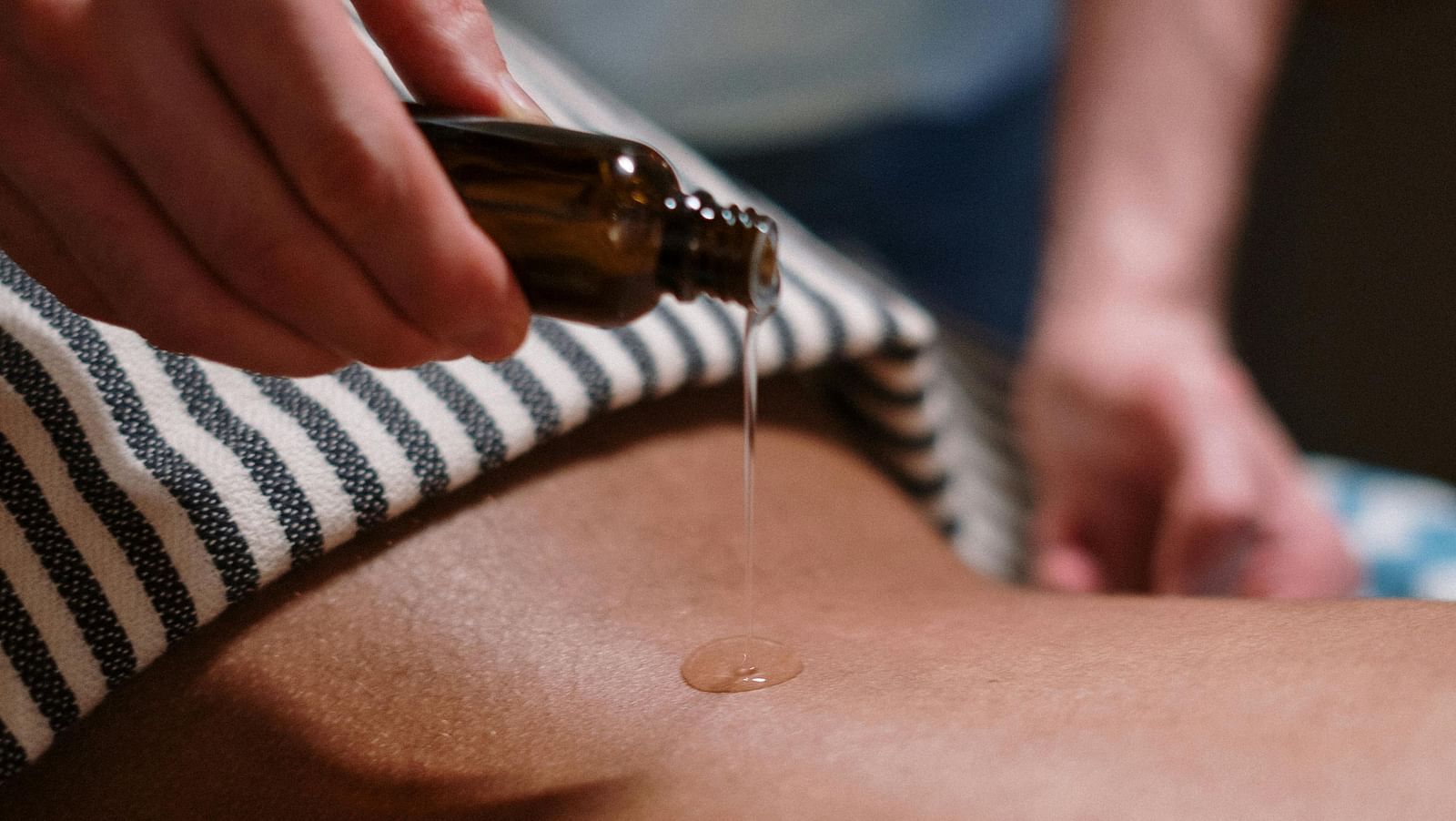 A person pouring essential oil from a vial on a person's back for a therapeutic massage.