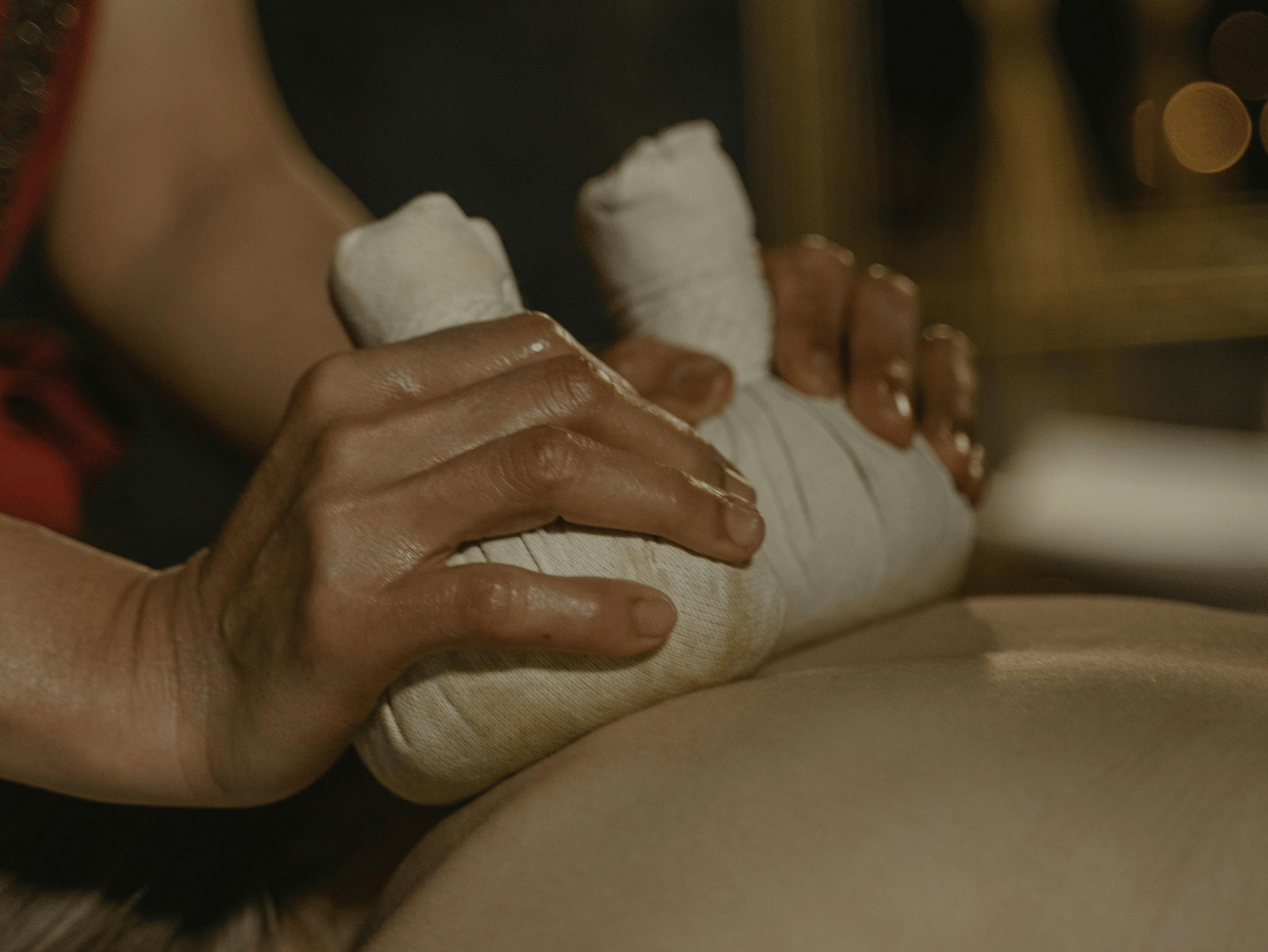 A masseuse using cloth bundles to press the back of a person.