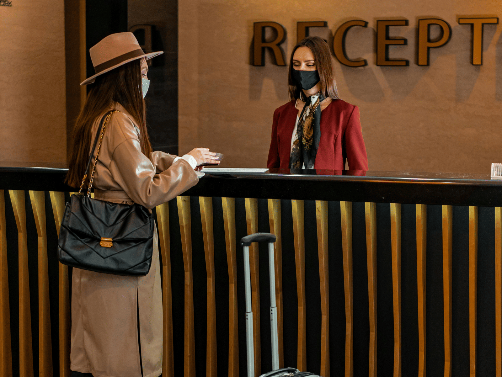 A woman standing at the front desk with her luggage, while a hotel attendant assists her from behind the desk.