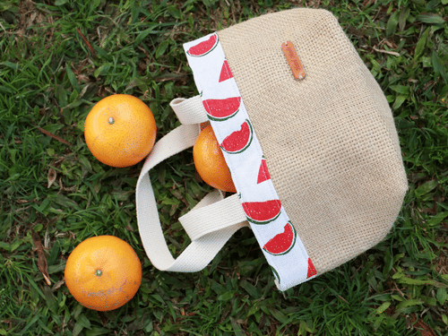 A jute handbag on a manicured garden with mandarins next to it