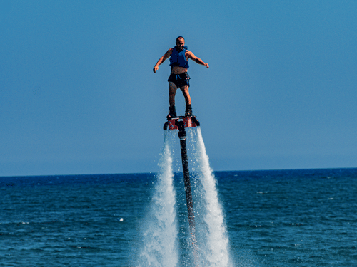 A rider flyboarding, equipped with gears and bright bly sky in the background.
