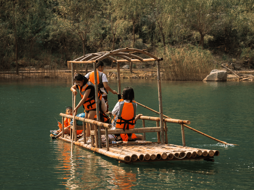 Visitors enjoying a peaceful bamboo rafting experience on calm waters surrounded by lush forests and scenic natural beauty.