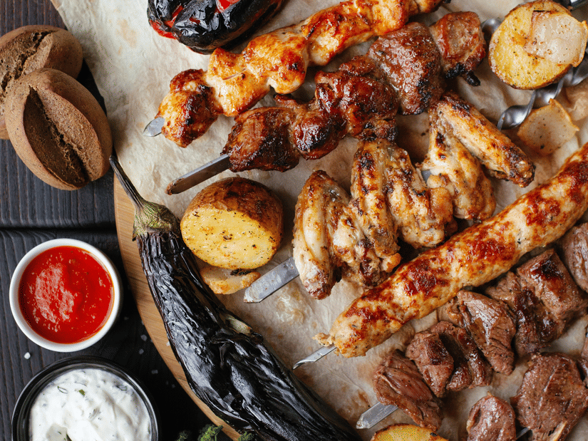 Platter of grilled kebabs served with dips and fresh vegetables.
