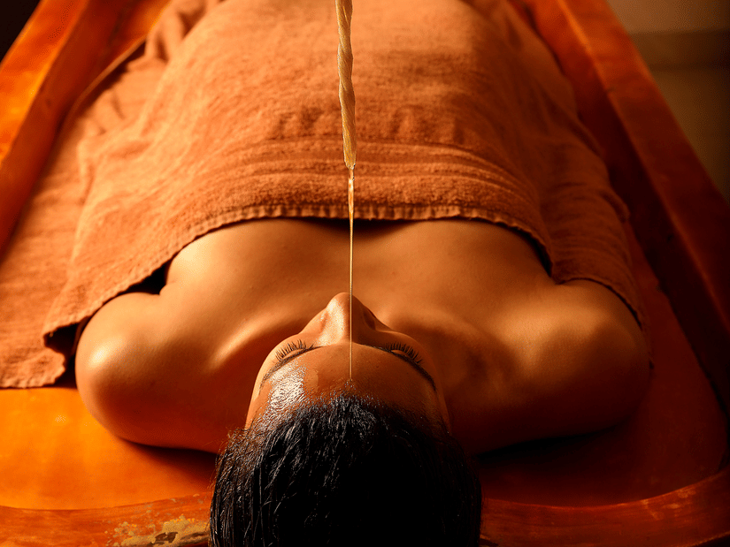 A person lying on a table receiving an Ayurvedic oil therapy on the forehead at Heritage Village Resorts & Spa, Manesar, one of the best luxury spa resorts near Delhi