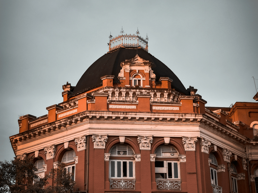 A grand heritage building in red brick featuring a dark domed roof and Victorian architectural details against a cloudy sky