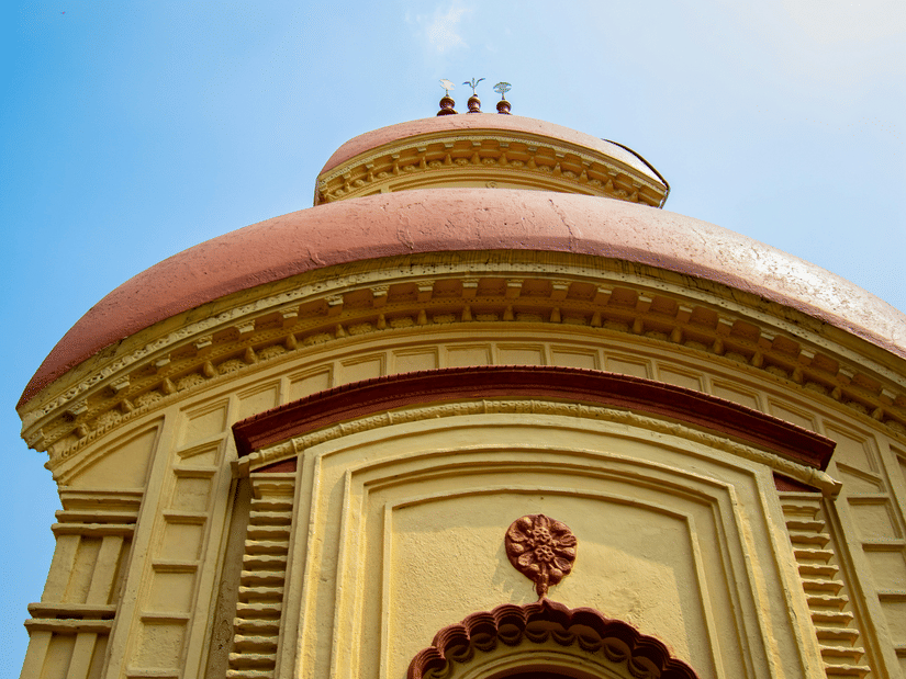 A traditional terracotta temple spire with curved roofs against a clear blue sky