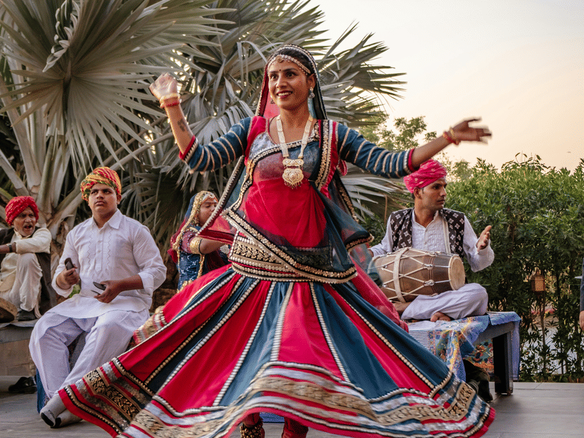 Kalbelia dancer twirls gracefully beside palm trees, colourful skirt spreading dramatically in front of the musicians