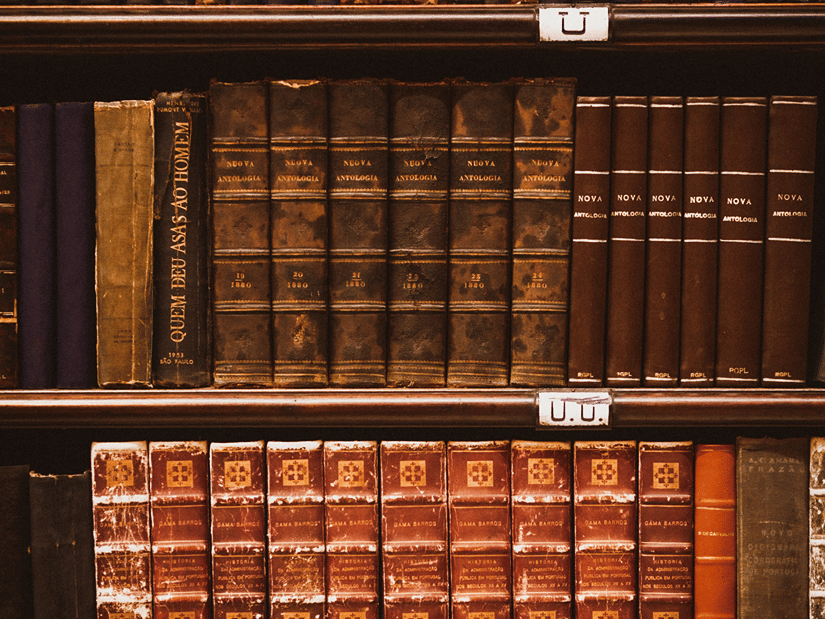Shelves stacked with antique leather-bound books in a dimly lit library or archive.