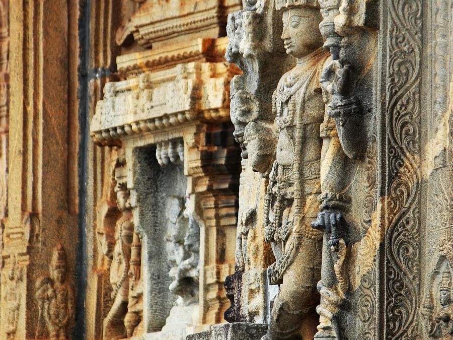  A weathered stone pillar and wall intricately carved with figures and designs, part of an ancient structure.