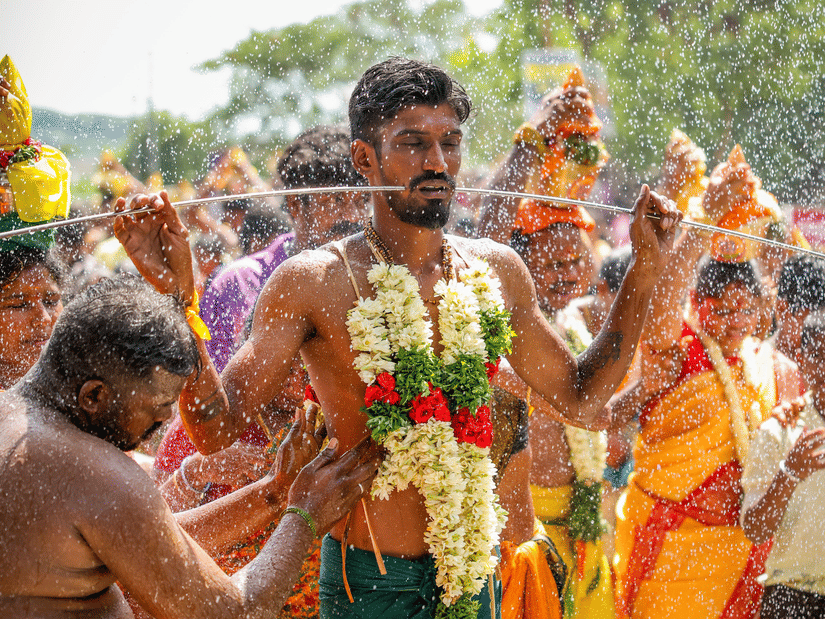 A devotee carrying a Kavadi on his shoulders with a pierced cheek during a traditional Hindu religious festival ritual.