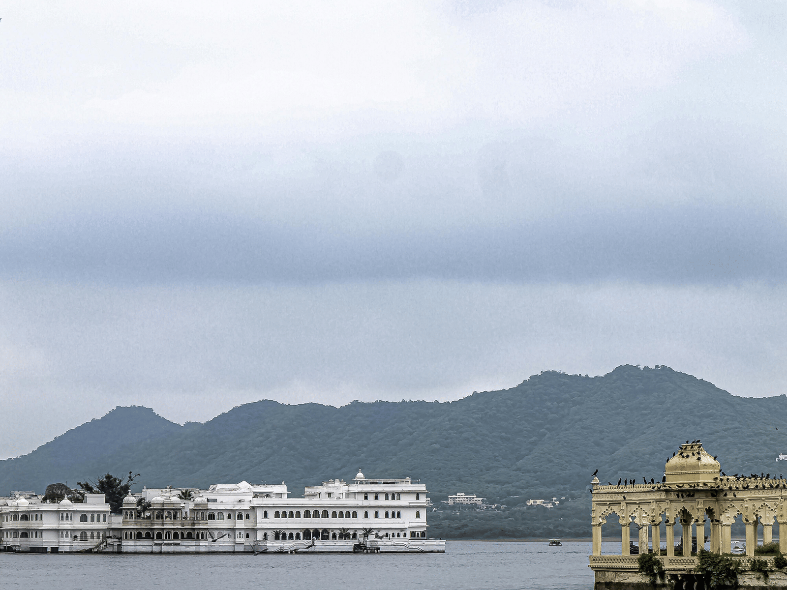 White palatial buildings stand on the edge of a serene lake under an overcast, cloudy sky.
