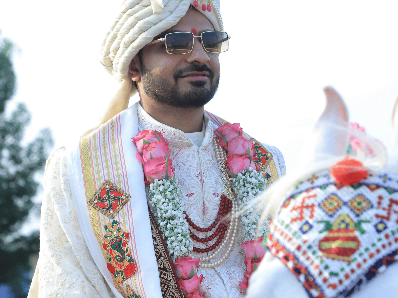 A groom dressed in traditional attire holding ceremonial items during a vibrant outdoor Indian wedding celebration.