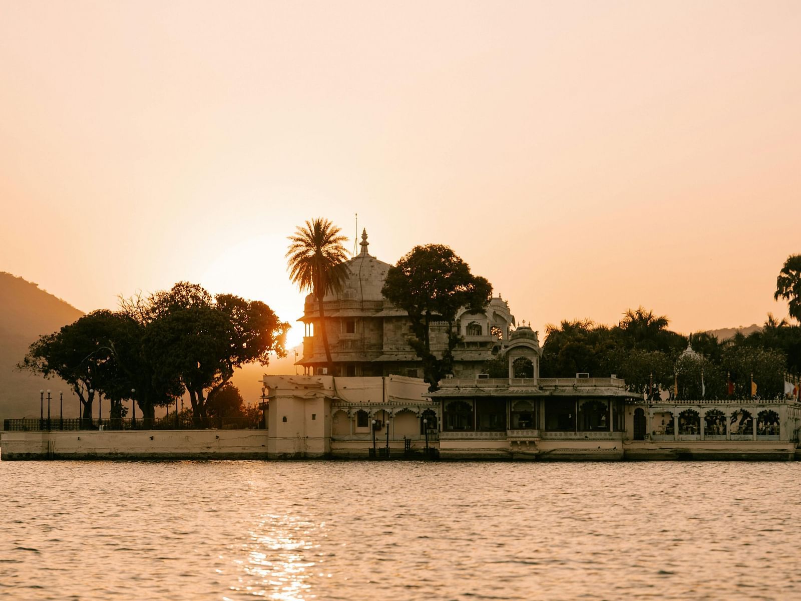 White building with royal architecture surrounded by trees on a water body at sunset 
