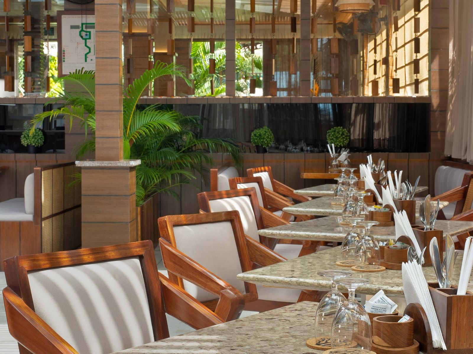 5th Bistro Cafe and Bar at Coral Reef Resort & Spa in Havelock featuring a dining area with outdoor seating, featuring wooden tables and striped chairs. The space is set in a lush garden with ample greenery, creating a comfortable, scenic setting - Coral R