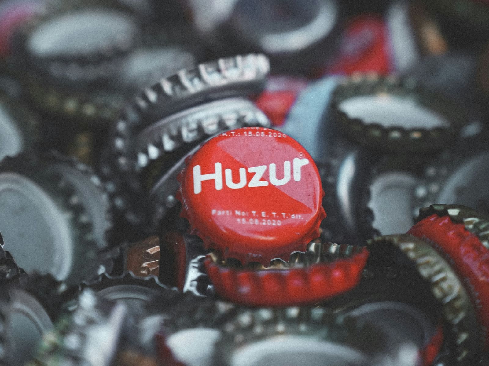 A close up shot of many bottle caps kept together with a bottle cap having the words Huzur.