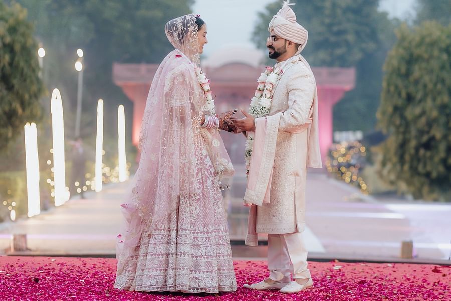 Bride and groom walking hand in hand on a flower-covered platform above water.