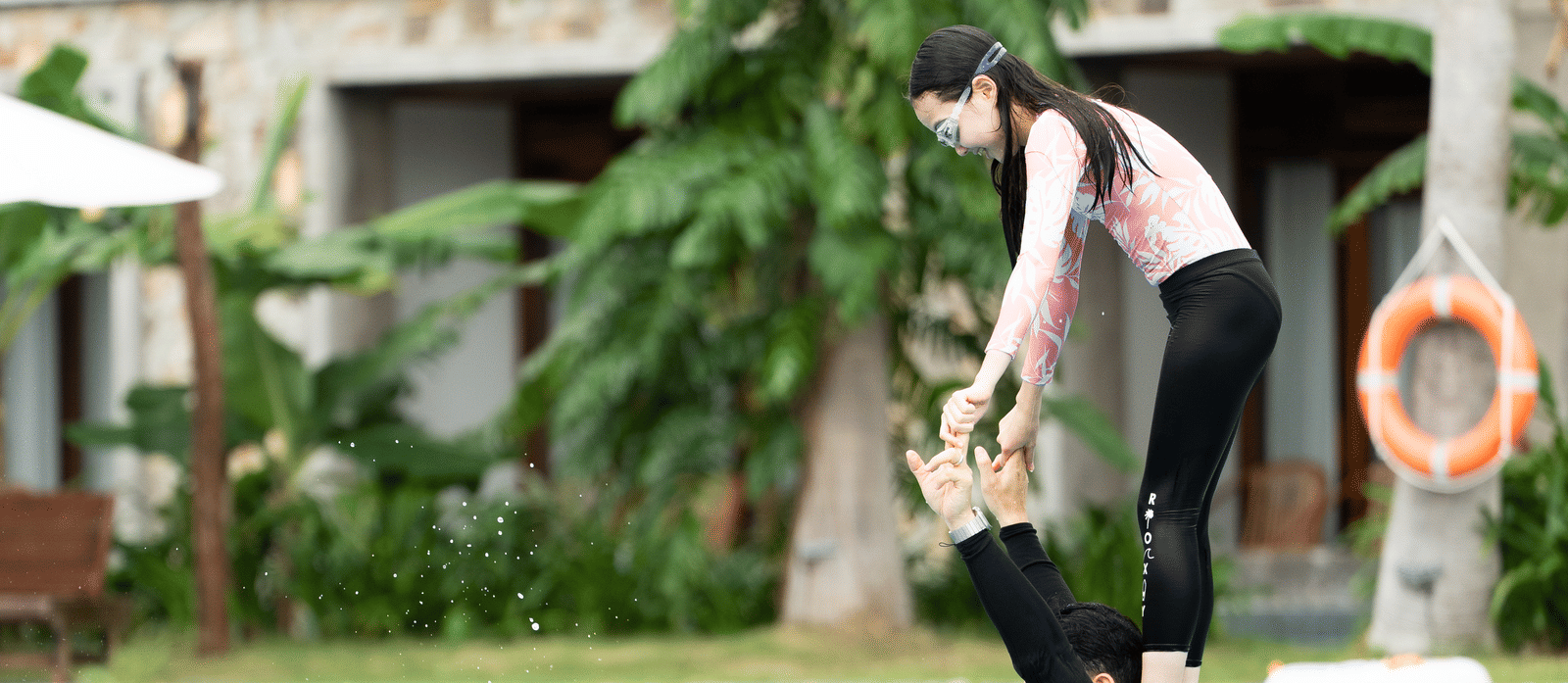 A woman standing on a shoulder of a man who is in a swimming pool