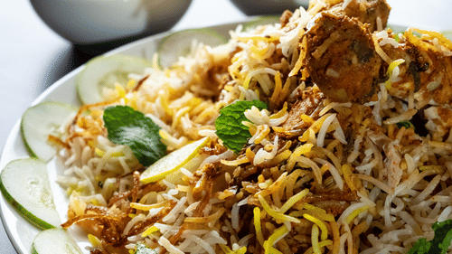 Plate of biryani with fried onions and green garnish, accompanied by curry bowls.