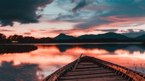 a close up shot of the front of the boat with an island in the background and different hues in the sky