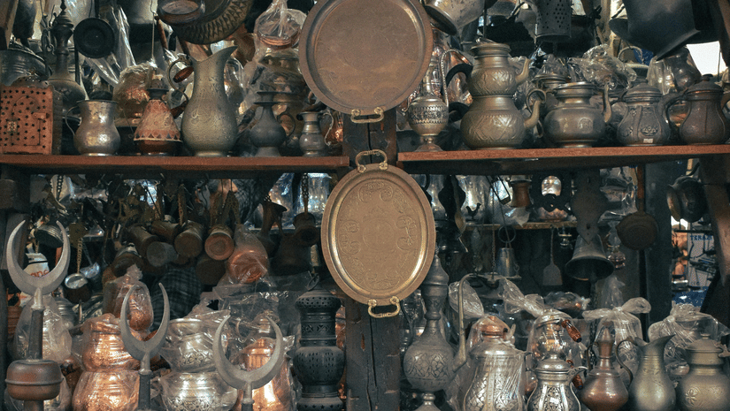 Shelves in a shop crowded with various metal vessels, plates, and decorative objects made of copper, brass, and silver.
