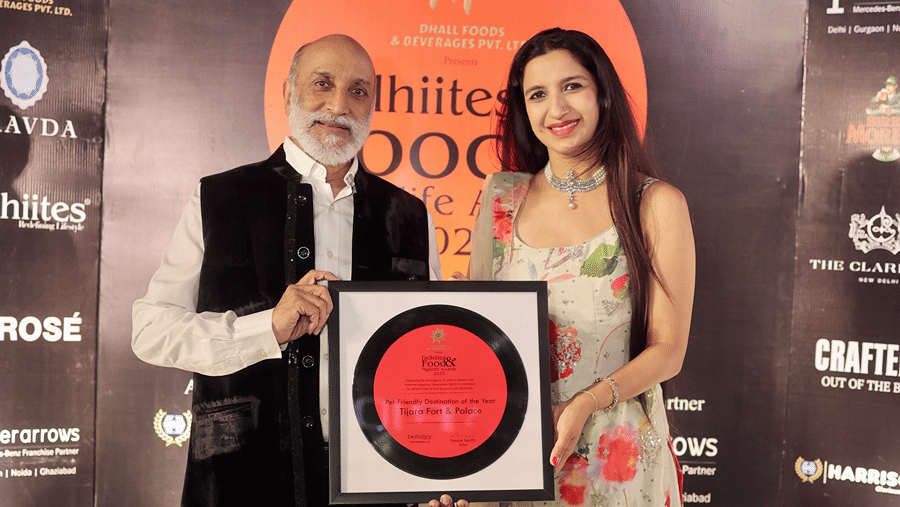Two people posing with a framed award for 'Pet-Friendly Destination of the Year 2025' awarded to Tijara Fort & Palace at the Delhiites Food & Nightlife Awards.